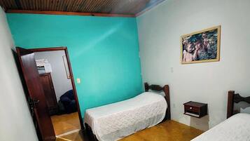 Una habitación con techo de madera, ventilador de techo, cama con cubrecama blanco, mesita de noche y un cuadro en la pared.