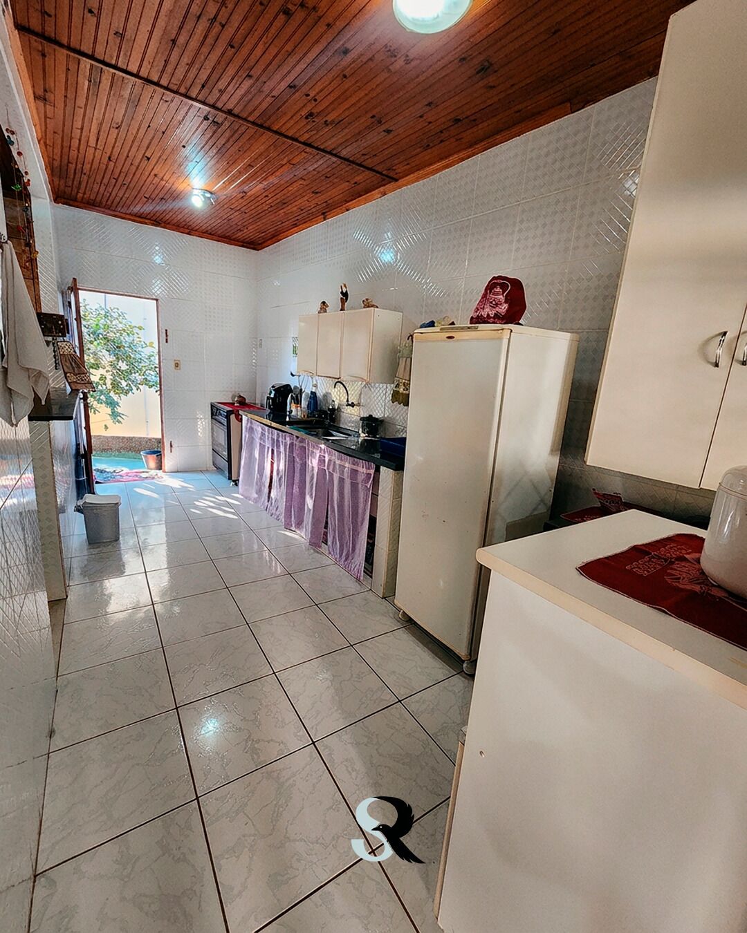 Una cocina con alacenas blancas, un refrigerador y piso de baldosas.