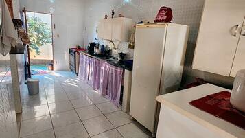Una cocina con alacenas blancas, un refrigerador y piso de baldosas.