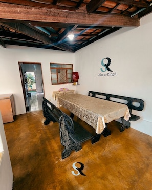 A room with a wooden bench, a table with a patterned tablecloth, a wall-mounted radiator, and a door leading outside.