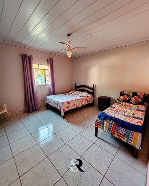 A bedroom with two beds, a ceiling fan, and a window with curtains.