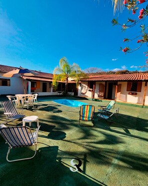 A pool area with lounge chairs and a small table, surrounded by buildings with tiled roofs.