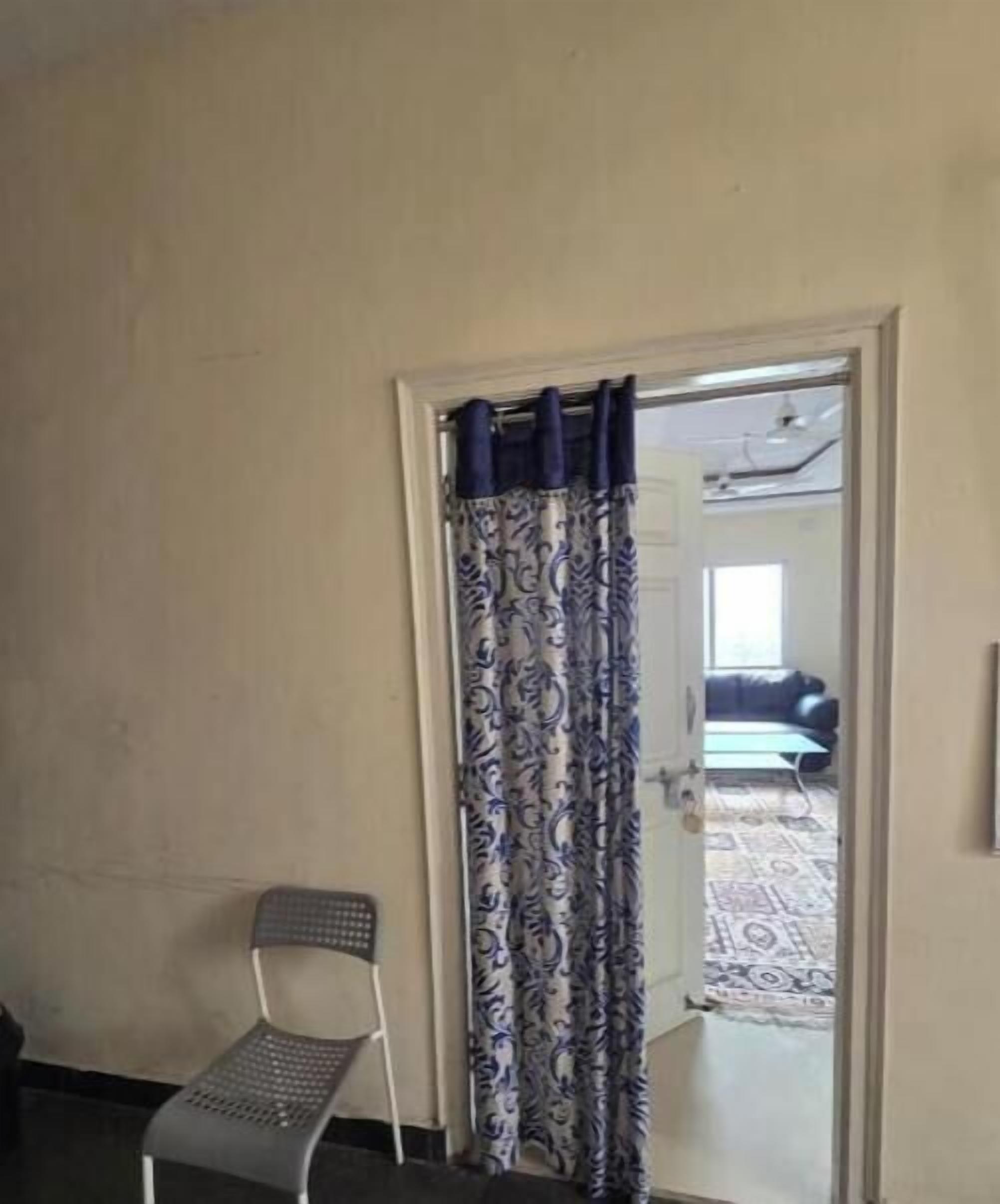 Une pi èce avec une porte donnant sur un autre espace, une chaise et un rideau à motifs.