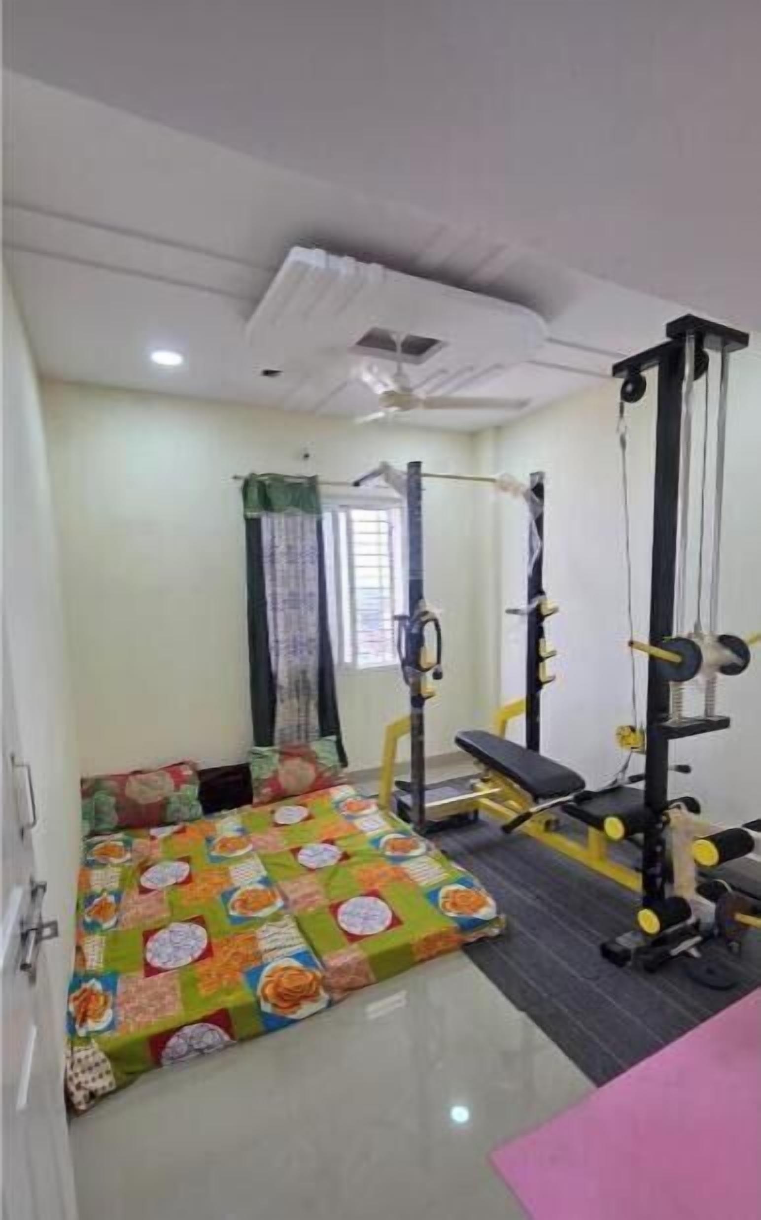 Une salle de sport équipée de matériel d’exercice, avec un tapis de sol à motifs et un ventilateur au plafond.