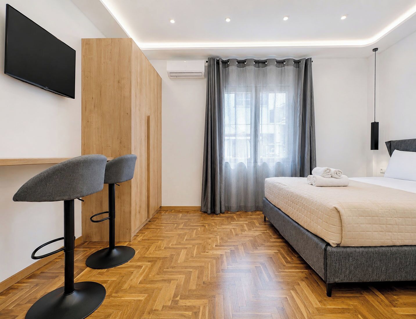 A modern hotel room with a bed, a TV, a desk with two chairs, and a window with curtains.