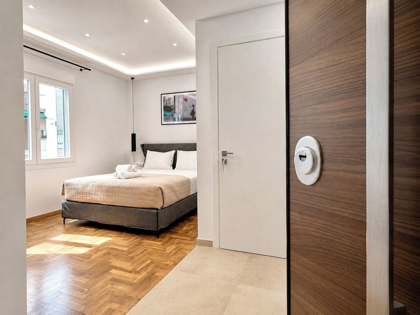 A modern hotel room with a bed, a wooden door, and a view of the outside.