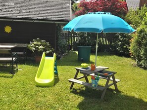 Un giardino sul retro con uno scivolo, un tavolo da picnic e un ombrellone.
