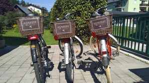 Tre biciclette parcheggiate su una superficie pavimentata con cestini fissati al portapacchi posteriore, recanti l'etichetta 'AUSZEIT Kaffee'.