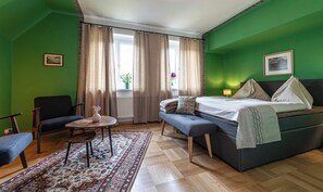 Una stanza con un letto, una sedia, un tavolino con un vaso e una finestra con tende.