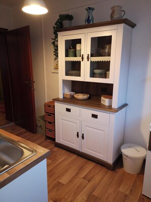 Una cucina con mobili bianchi, un piano di lavoro in legno e un lavello. Si vedono cesti e un cestino.