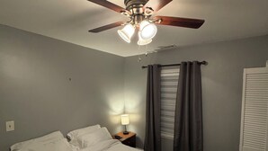 A bedroom with a bed, a nightstand, a ceiling fan, and a window with curtains.