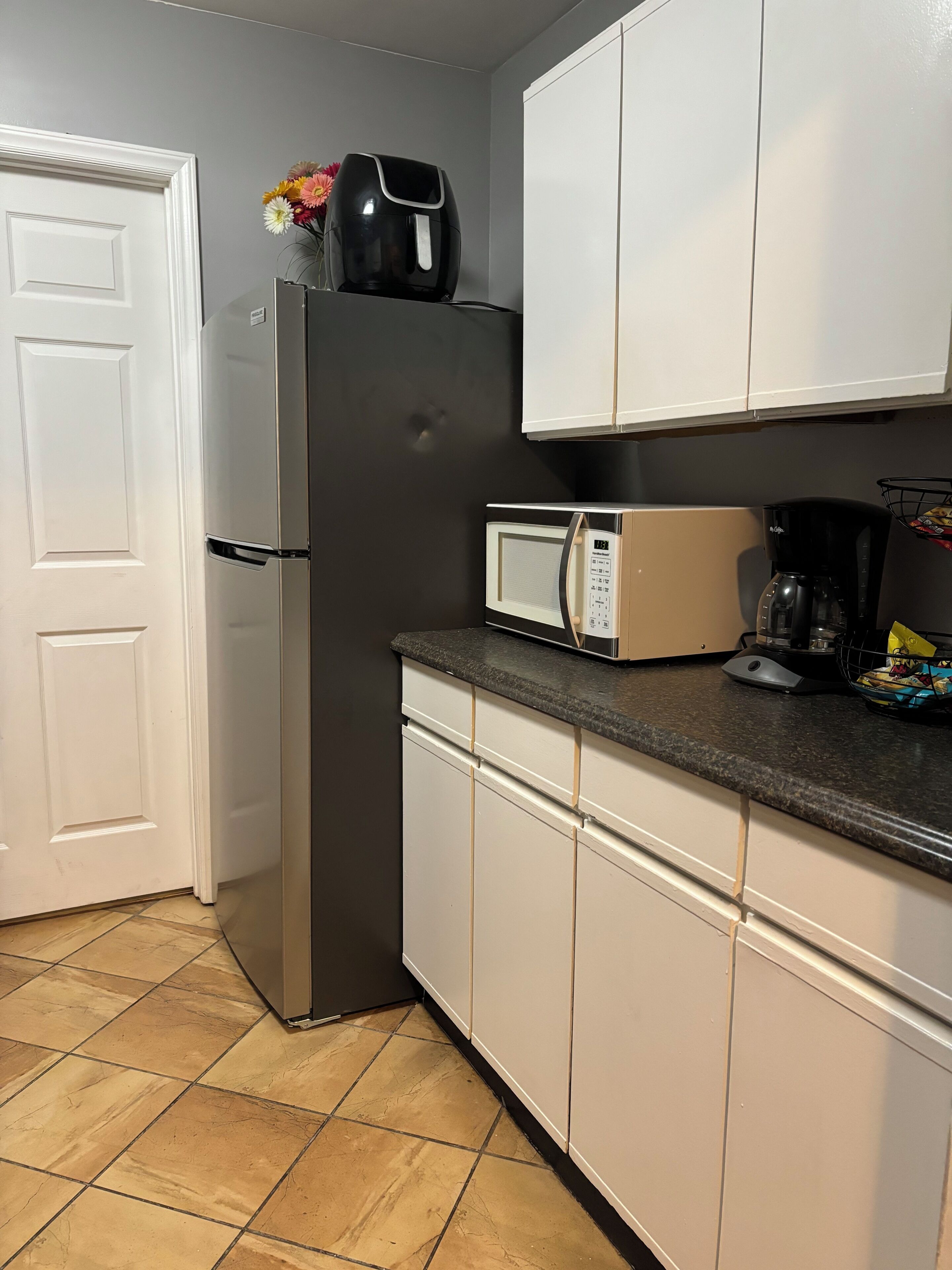 A kitchen with a refrigerator, microwave, coffee maker, and a flower vase on the counter.