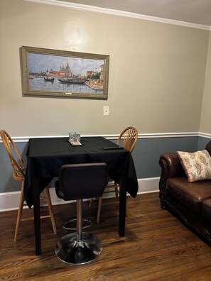 A dining area with a table set for four, a chair, a remote control, and a decorative item on the table. - Charming 2BR Bungalow/Walkable Chantilly & Plaza Midwood Front Half of Home (Charlotte)