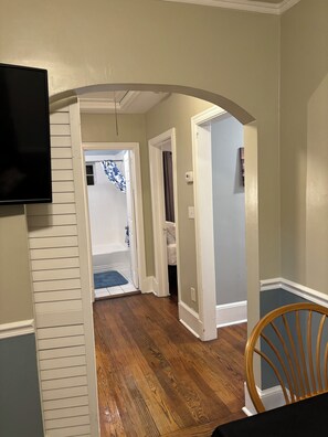 A hallway with a wooden floor, a television mounted on the wall, and a chair. - Charming 2BR Bungalow/Walkable Chantilly & Plaza Midwood Front Half of Home (Charlotte)