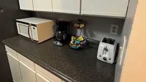 A kitchenette with white cabinets, a microwave, a coffee maker, a toaster, and a basket of snacks.