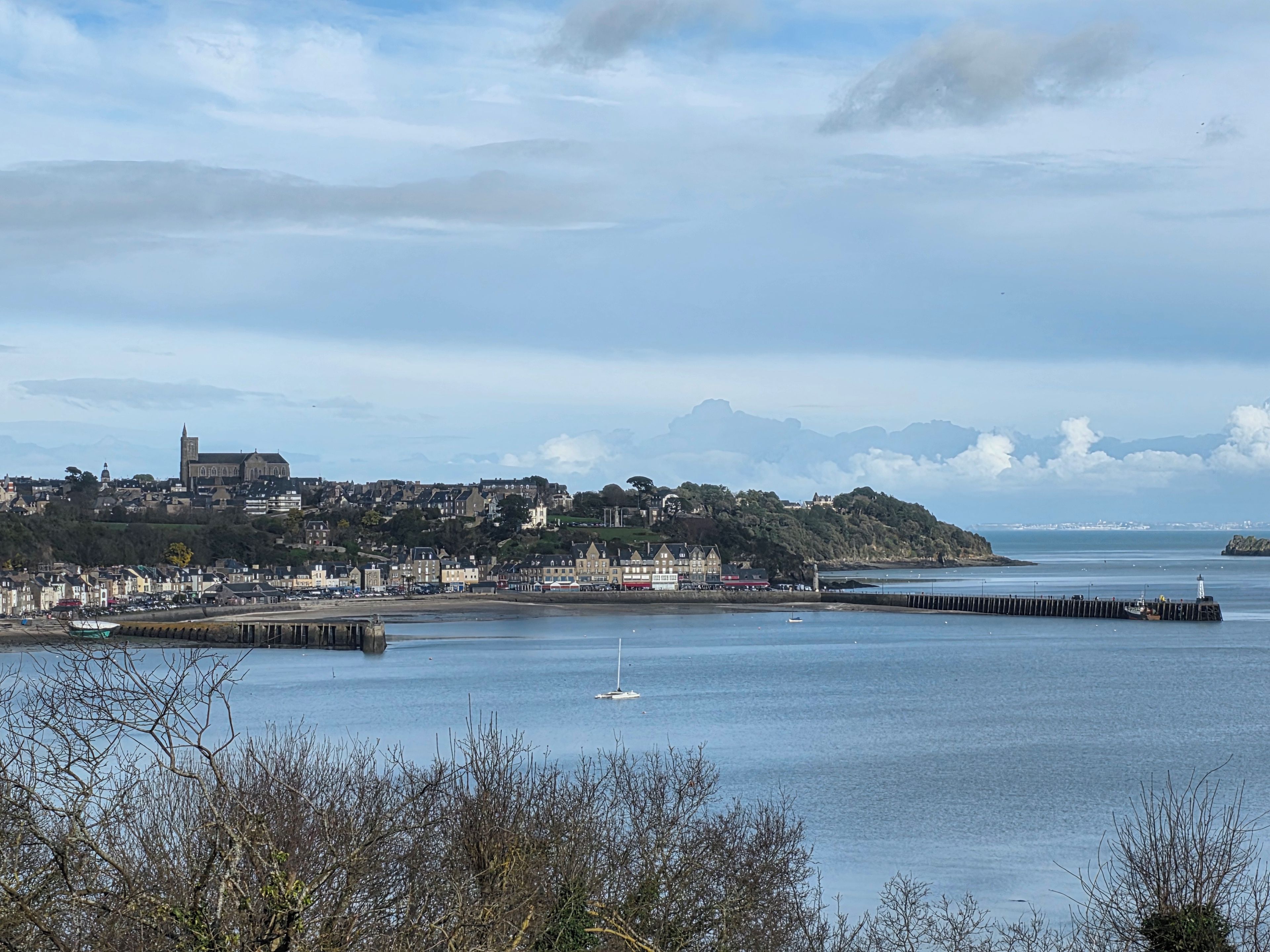A coastal town with a prominent church, a pier extending into the water, and a clear sky.
