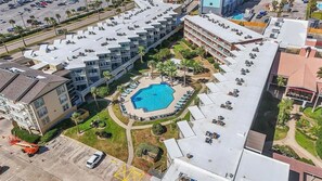 A multi-story hotel with a rooftop pool surrounded by lounge chairs and palm trees. - Ocean Front Condo - 2 pools hot tub Cruise Parking on seawall babes beach (Galveston)