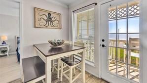 A dining area with a table and chairs, a decorative wall piece, and a view through a door to the outside. - Ocean Front Condo - 2 pools hot tub Cruise Parking on seawall babes beach (Galveston)