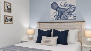 A neatly made bed with a blue and white patterned throw, two bedside lamps, and a framed artwork of an octopus on the wall. - Ocean Front Condo - 2 pools hot tub Cruise Parking on seawall babes beach (Galveston)