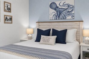 Ein ordentlich bezogenes Bett mit einer blau-weißen Tagesdecke, zwei Nachttischlampen und einem gerahmten Bild von einem Oktopus an der Wand.