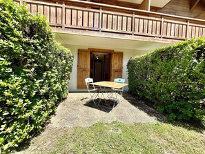 Eine überdachte Terrasse im Freien mit Holztisch und Stühlen, umgeben von üppigem Grün.