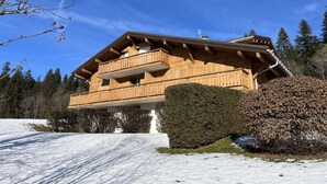 Um chalé de madeira com varanda, rodeado por neve e árvores.