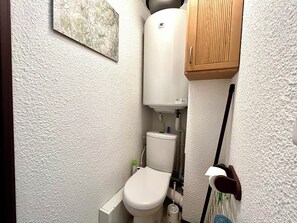 Ein kleines Badezimmer mit Toilette, einer weißen Wand und einem Holzschrank.