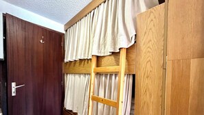 Um quarto com uma cama beliche de madeira, uma escada, uma porta e cortinas.