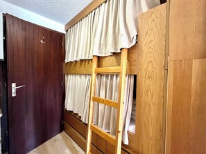 Ein Zimmer mit einem hölzernen Etagenbett, einer Stehleiter, einer Tür und Vorhängen.