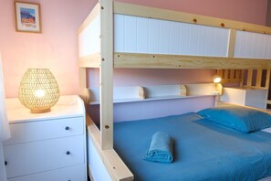 Ein Etagenbett mit Holzrahmen, ein Nachttisch mit Lampe und eine blaue Bettdecke.