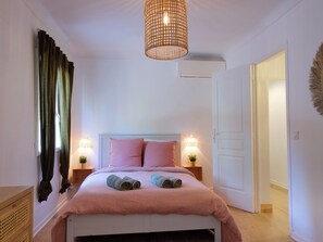 Um quarto com cama, duas luminárias de cabeceira, um lustre e uma porta.