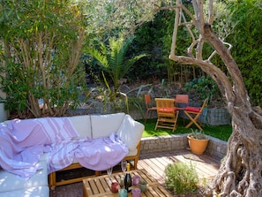 A patio with a white sofa, wooden chairs, a table with drinks, and a potted plant. - The Villa Under the Stars – Les Issambres (Roquebrune-sur-Argens)