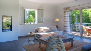 A modern living room with a sofa, coffee table, and a view of the outdoors through large windows. - Villa Les Issambres avec Piscine,10 Pers (Roquebrune-sur-Argens)
