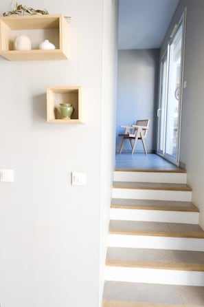 A staircase with wooden steps leading to a room with a chair and a table, and two wooden shelves with decorative items. - The Villa Under the Stars – Les Issambres (Roquebrune-sur-Argens)