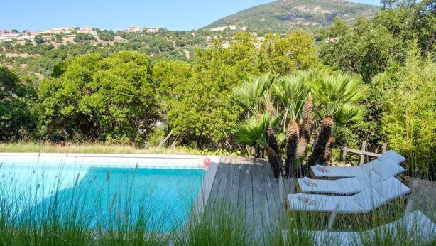 A swimming pool with a wooden deck and lounge chairs, surrounded by lush greenery and a mountainous backdrop. - Villa Les Issambres avec Piscine,10 Pers (Roquebrune-sur-Argens)