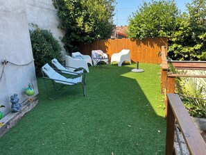 A backyard with artificial grass, a wooden fence, and outdoor furniture including lounge chairs and a table. - Cozy house near the beach and Arcachon town centre (Arcachon)
