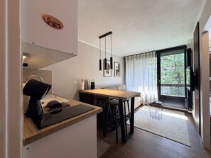 Een kleine keuken met een houten aanrecht, een inbouwfornuis en een eethoek met een tafel en stoelen.