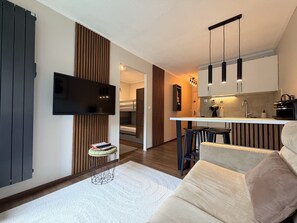Ein modernes Wohnzimmer mit einer Couch, einem an der Wand befestigten Fernseher und einer Küchenzeile mit einer Bar.
