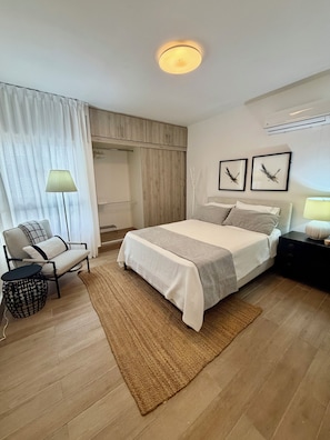 A hotel room with a bed, a chair, a bedside table, a lamp, a wardrobe, and two framed pictures on the wall.