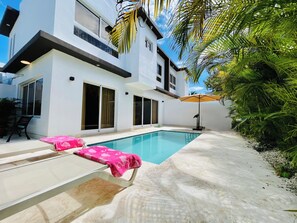 A modern two-story house with a swimming pool, outdoor furniture, and a patio area.