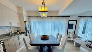 A modern dining area with a large table, white chairs, and a chandelier.
