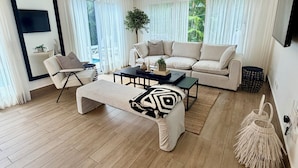 A modern living room with a sofa, coffee table, and a large window with curtains.