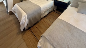 A hotel room with two beds, a wardrobe, a nightstand with a lamp, and an air conditioning unit.