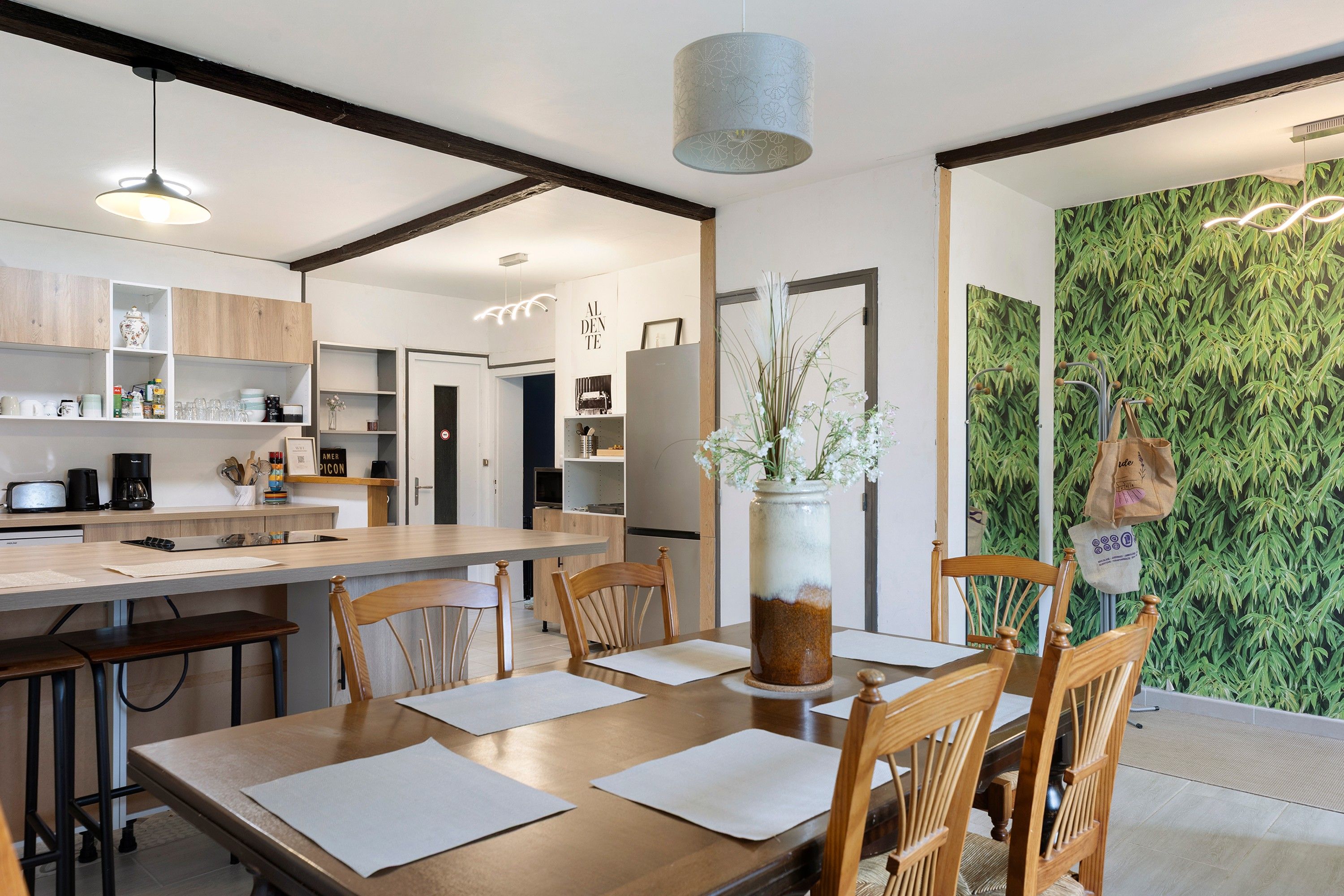 Une cuisine moderne avec des meubles en bois, une table à manger avec des chaises et un mur vert agrémenté d’un décor en bambou.