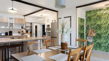 Une cuisine moderne avec des meubles en bois, une table à manger avec des chaises et un mur vert agrémenté d’un décor en bambou.