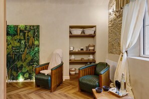 A room with two leather chairs, a wooden floor, a shelf with baskets, and a wall with a textured pattern.