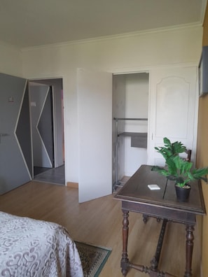 Een kamer met een bed, een kleine tafel met een plant en een deur naar een andere kamer.