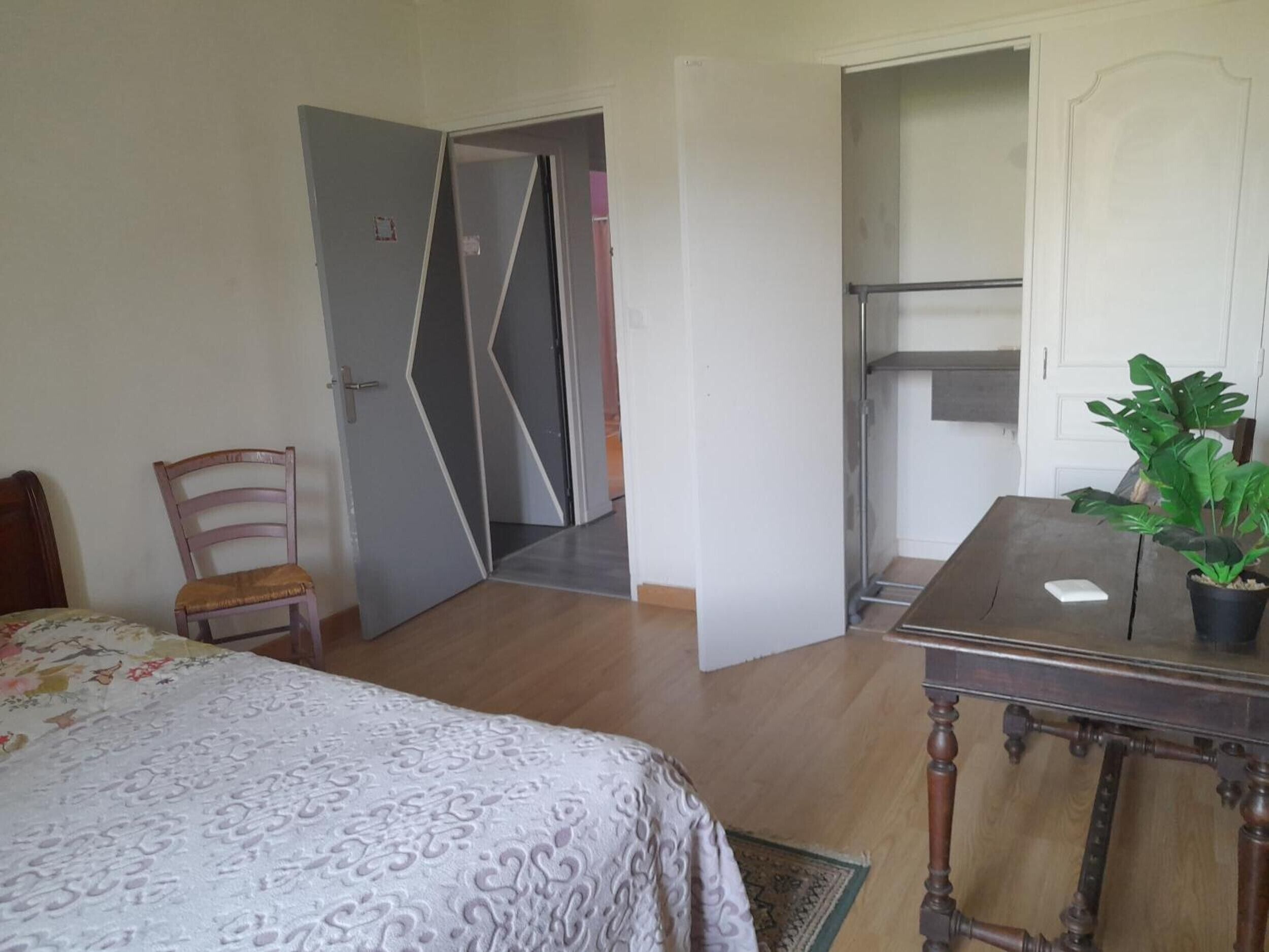A bedroom with a bed, a chair, a table with a plant, and a wardrobe.