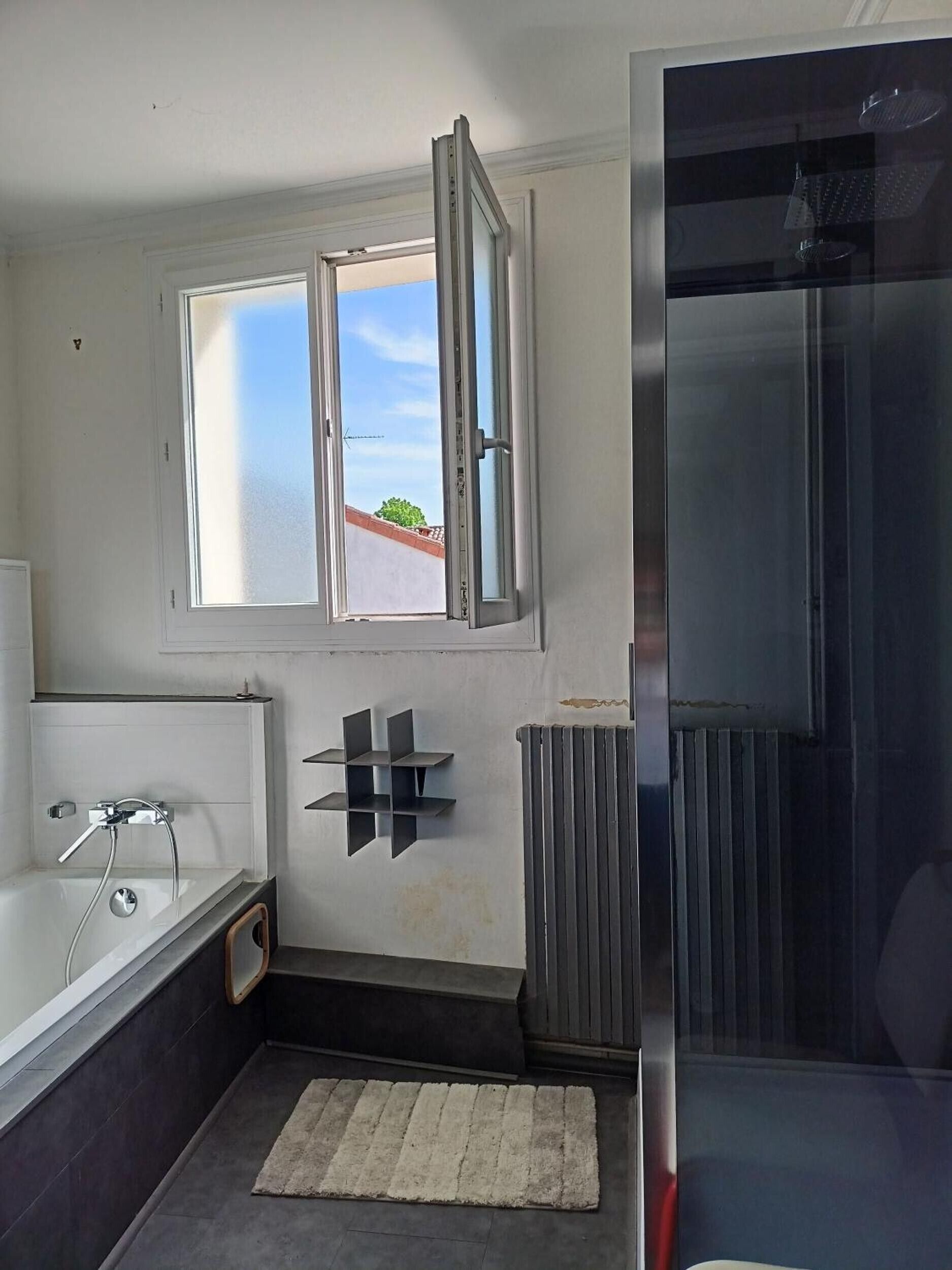A bathroom with a bathtub, a window, a radiator, and a shower area.