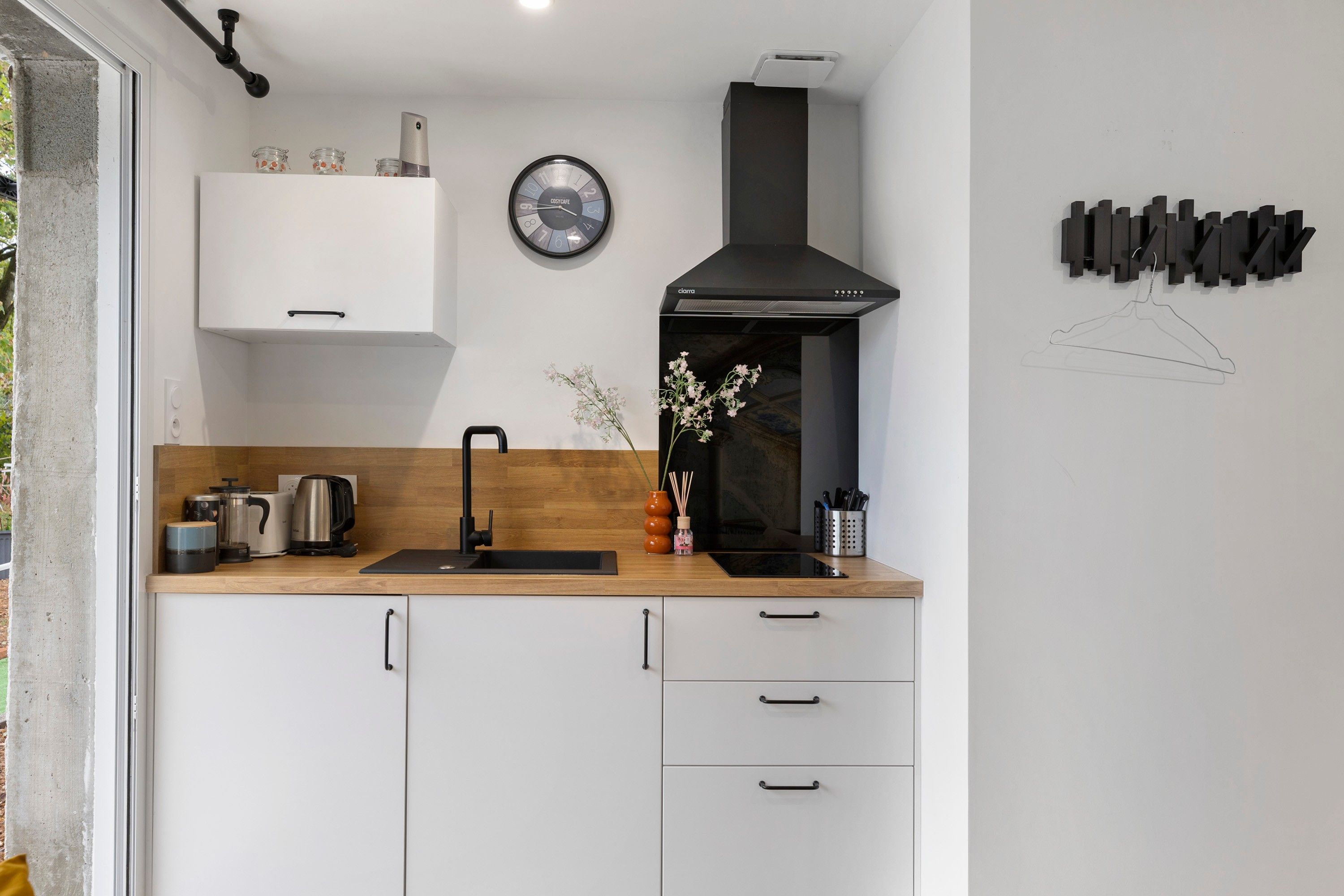 A modern kitchen with a black range hood, a clock, and a minimalist design.